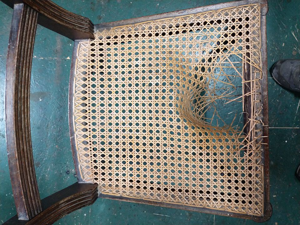 Close-up of a hand-caned seat with a broken, sagging section before recaning